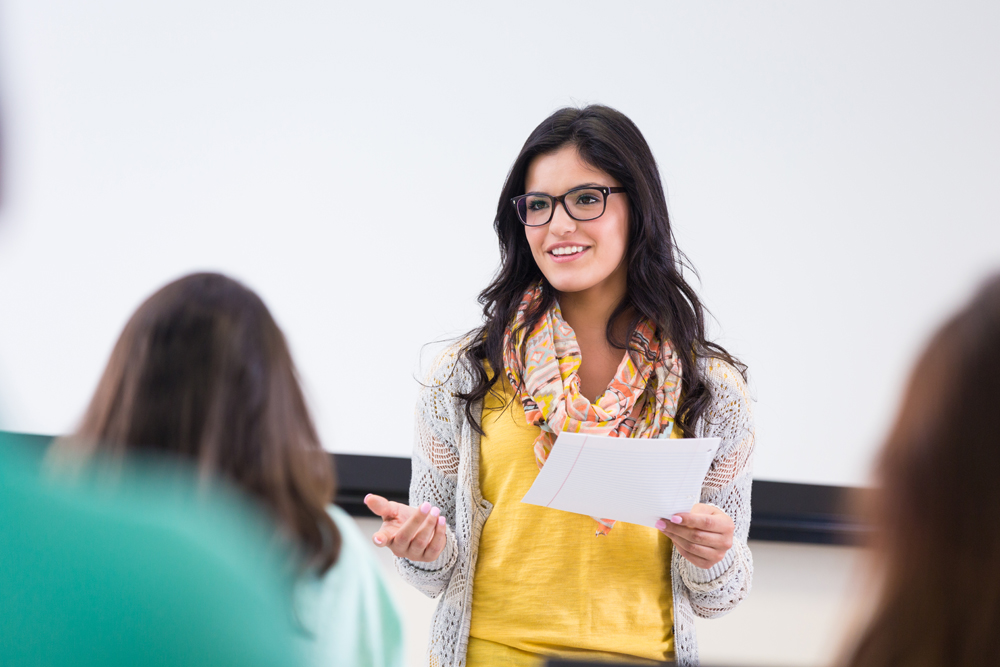 Cute hipster student reading report in front of classmates